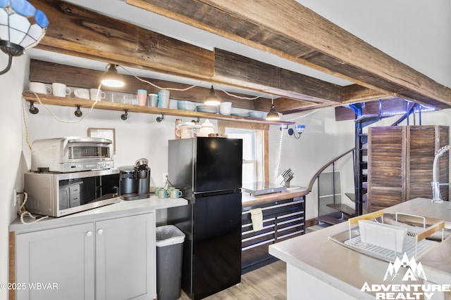 kitchen with beamed ceiling, light wood-style flooring, stainless steel microwave, freestanding refrigerator, and a toaster