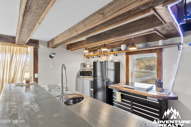 kitchen featuring freestanding refrigerator, a sink, stainless steel countertops, stainless steel microwave, and beamed ceiling