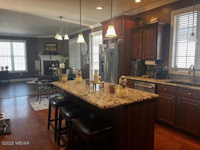 kitchen featuring dark wood-type flooring, sink, appliances with stainless steel finishes, a kitchen island, and pendant lighting