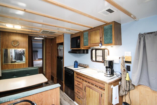 kitchen featuring black appliances, wooden walls, and light hardwood / wood-style flooring