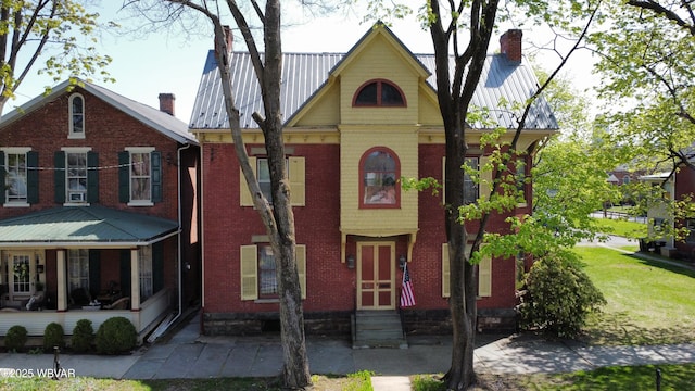 view of front facade with a chimney, entry steps, brick siding, and metal roof