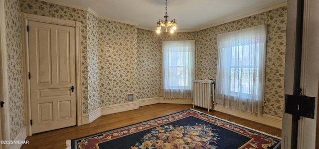 interior space with radiator, wood finished floors, ornamental molding, and an inviting chandelier