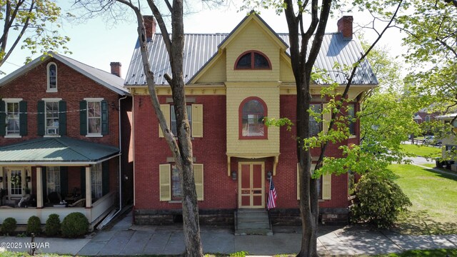 view of front of property featuring a chimney, brick siding, entry steps, and metal roof