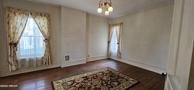 spare room featuring wood finished floors, crown molding, baseboards, and a notable chandelier