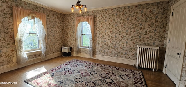 spare room featuring radiator heating unit, a chandelier, wood finished floors, and a healthy amount of sunlight