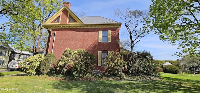 view of side of property with a lawn, a chimney, brick siding, and metal roof
