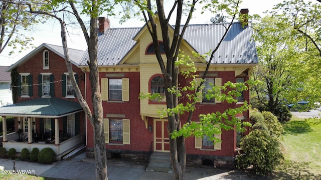 view of front facade with a chimney, entry steps, brick siding, and metal roof