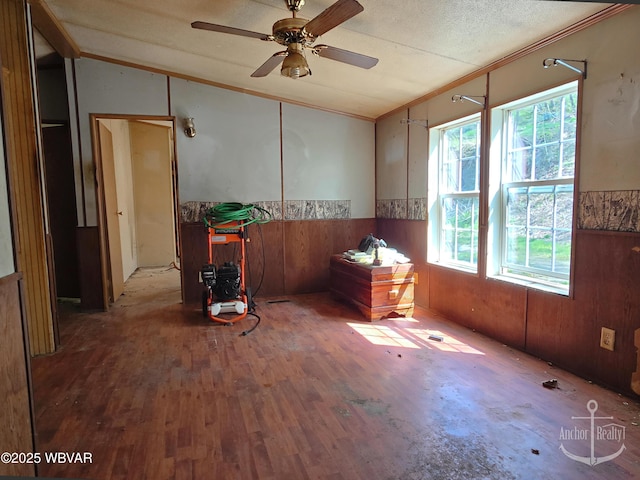 unfurnished room featuring crown molding, wood finished floors, lofted ceiling, ceiling fan, and a wainscoted wall