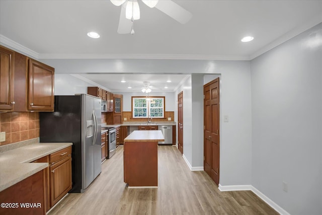 kitchen featuring a kitchen island, appliances with stainless steel finishes, ornamental molding, ceiling fan, and light hardwood / wood-style floors