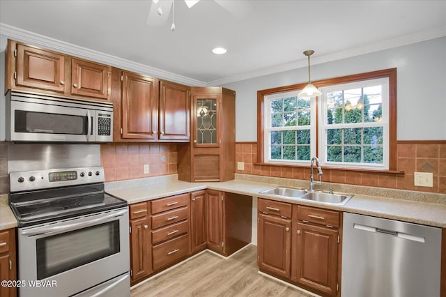 kitchen featuring sink, hanging light fixtures, stainless steel appliances, ornamental molding, and light wood-type flooring