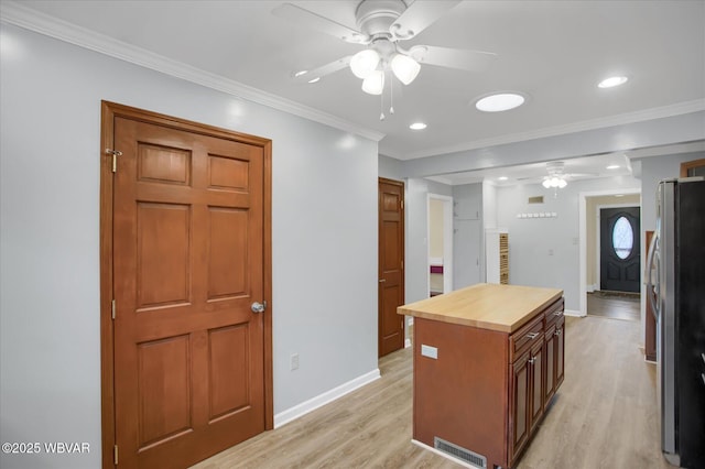 kitchen with light wood-type flooring, ornamental molding, stainless steel refrigerator, and a kitchen island