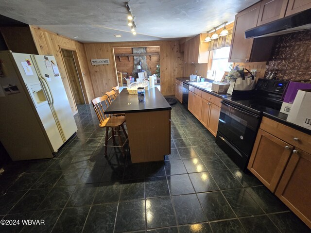 kitchen with black electric range oven, white refrigerator with ice dispenser, wooden walls, a kitchen island, and a kitchen bar