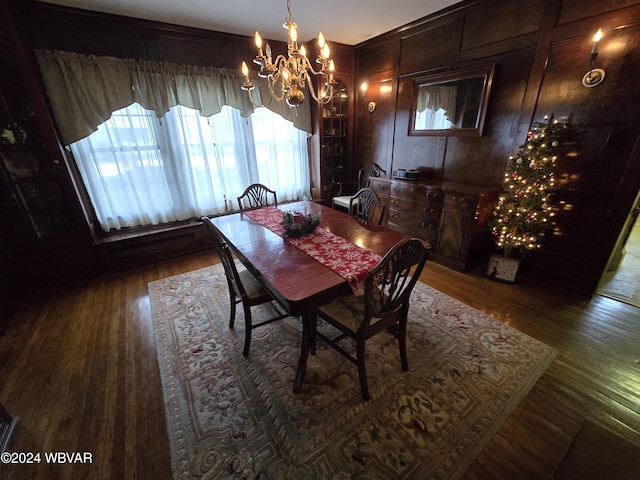 dining area with dark hardwood / wood-style floors, wooden walls, and a notable chandelier