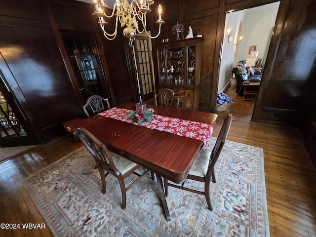 dining room with a chandelier, wood-type flooring, and wood walls