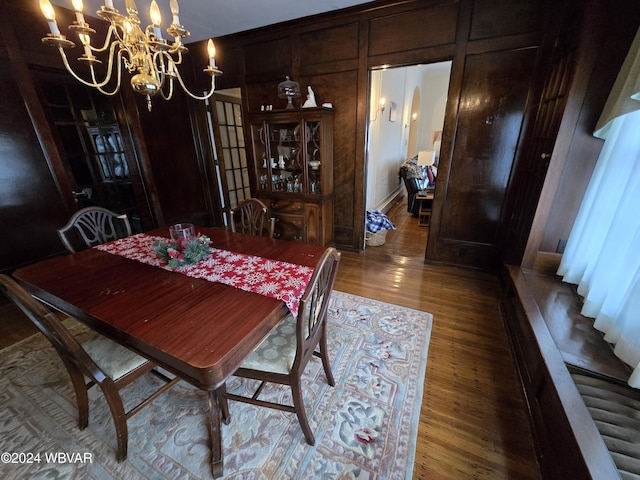 dining space with wooden walls, hardwood / wood-style flooring, and a notable chandelier