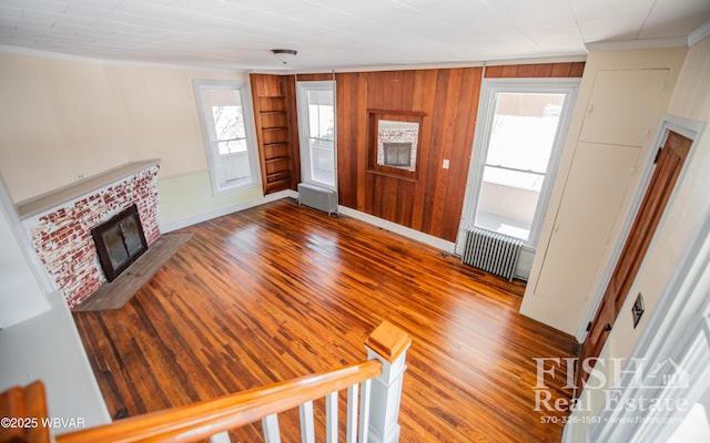 unfurnished living room with ornamental molding, wood-type flooring, radiator heating unit, and a fireplace