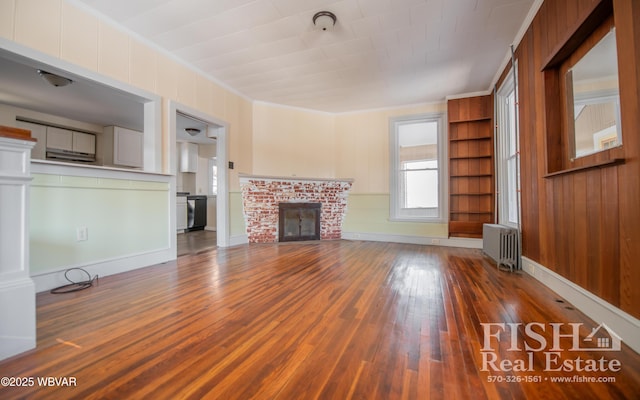 unfurnished living room featuring radiator, wood-type flooring, ornamental molding, and a brick fireplace