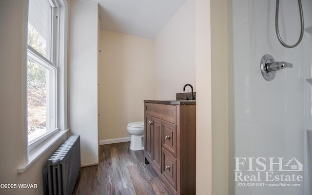 bathroom with radiator, a shower, wood-type flooring, vanity, and toilet