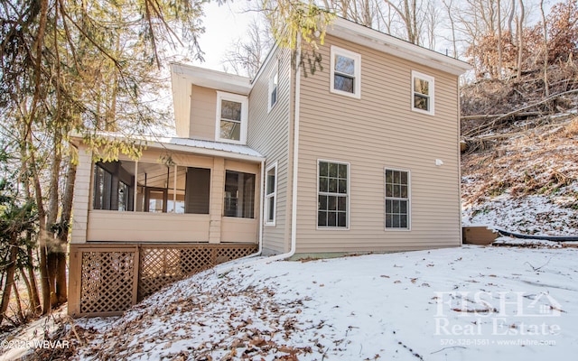 snow covered rear of property with a sunroom