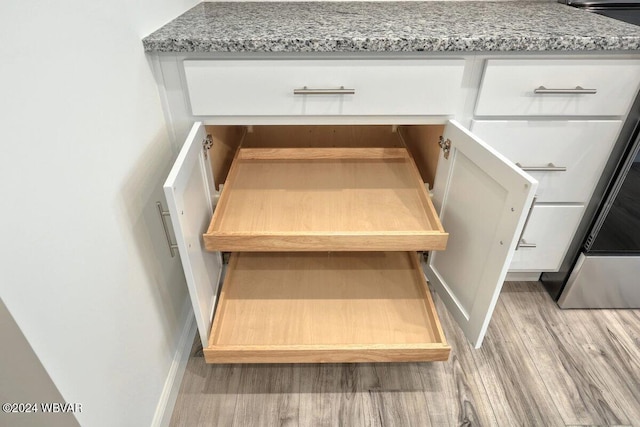 room details featuring light stone counters, white cabinets, and light wood-type flooring