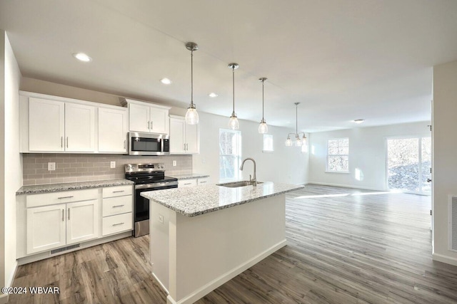 kitchen with stainless steel appliances, tasteful backsplash, an island with sink, decorative light fixtures, and white cabinets