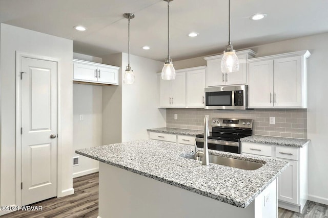 kitchen featuring an island with sink, white cabinets, stainless steel appliances, and decorative light fixtures