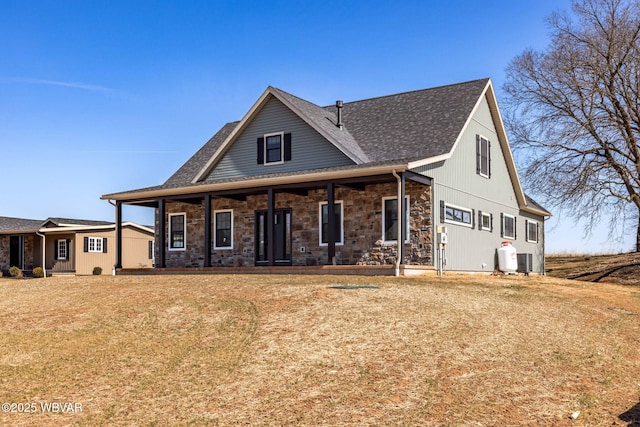 view of front facade with stone siding, central air condition unit, a shingled roof, and a front yard