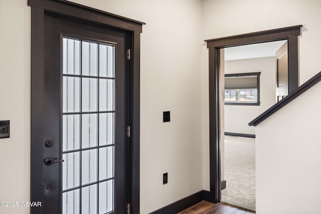 doorway featuring dark colored carpet, baseboards, and dark wood-style flooring