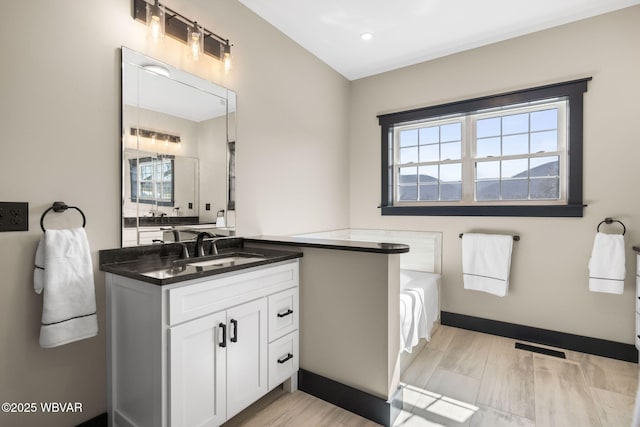 bathroom featuring baseboards, visible vents, vanity, and a garden tub