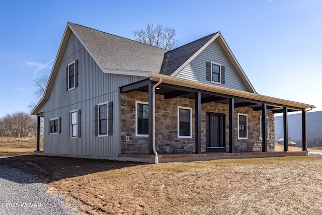 view of front of home featuring stone siding, covered porch, and roof with shingles