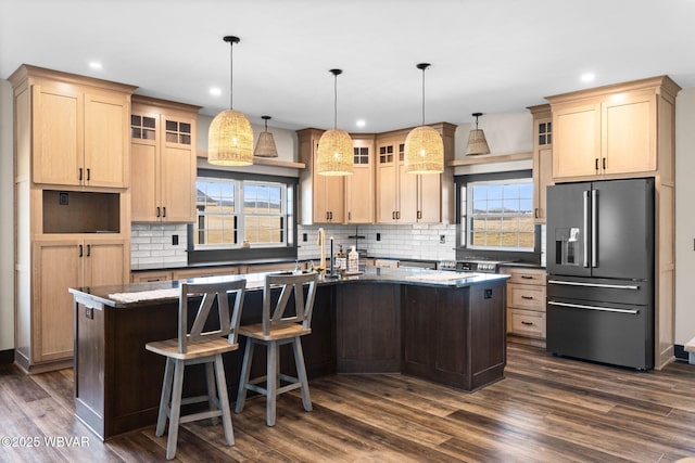 kitchen with dark wood-style floors, glass insert cabinets, high end fridge, and a kitchen island with sink