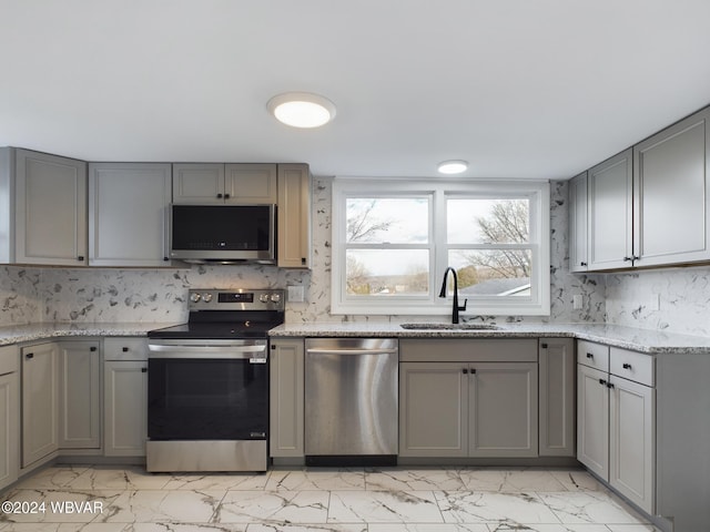 kitchen with light stone countertops, stainless steel appliances, gray cabinets, and sink