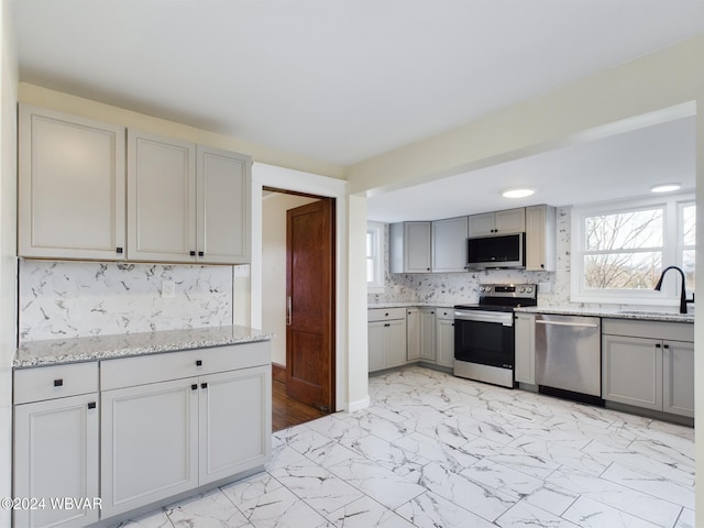 kitchen with light stone countertops, appliances with stainless steel finishes, tasteful backsplash, gray cabinetry, and sink