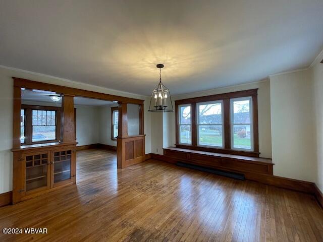 unfurnished living room with a chandelier, ornamental molding, baseboard heating, and dark wood-type flooring