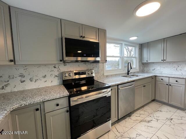 kitchen with stainless steel appliances, light stone counters, gray cabinetry, and sink