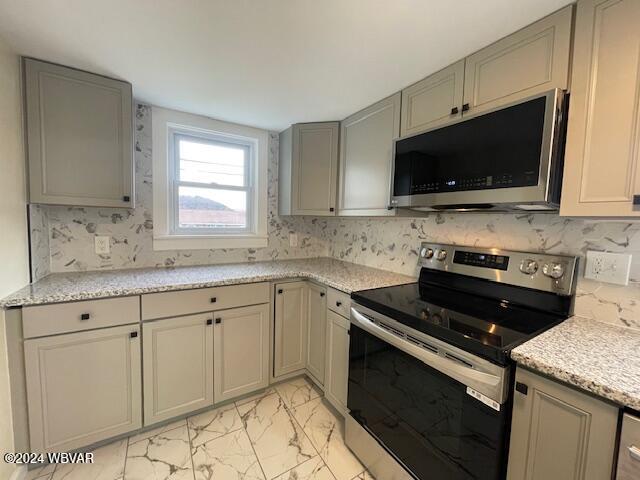 kitchen featuring appliances with stainless steel finishes, gray cabinets, and light stone counters