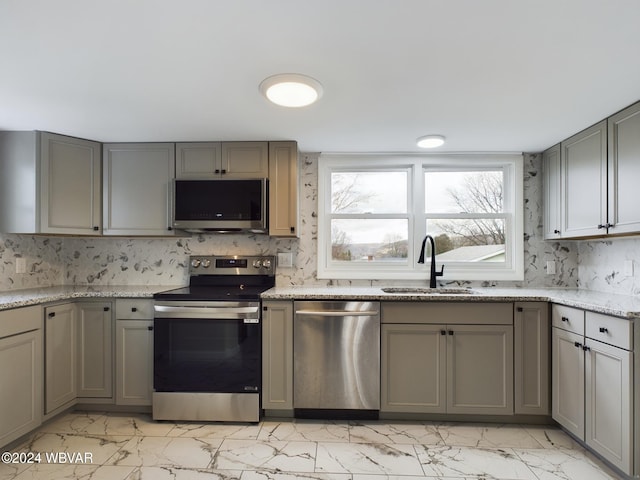 kitchen featuring stainless steel appliances, light stone counters, gray cabinetry, and sink