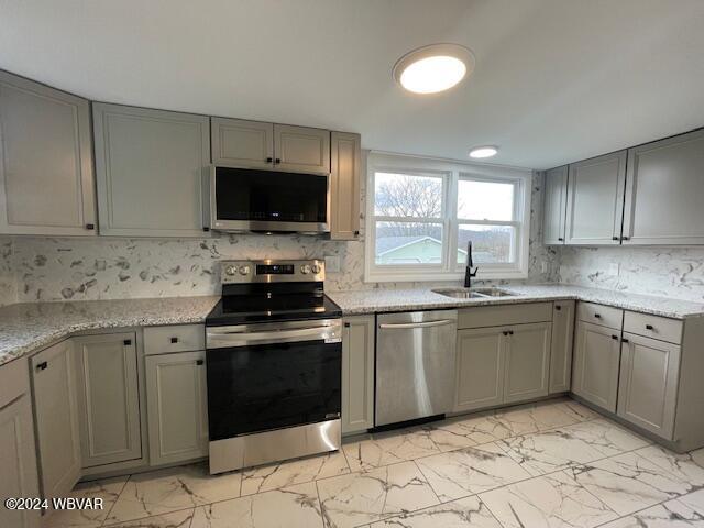 kitchen featuring light stone counters, gray cabinets, sink, and stainless steel appliances