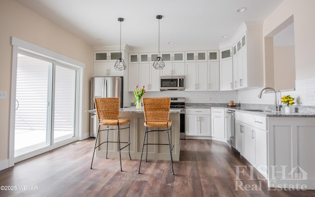 kitchen with white cabinets, a kitchen island, glass insert cabinets, stainless steel appliances, and a sink