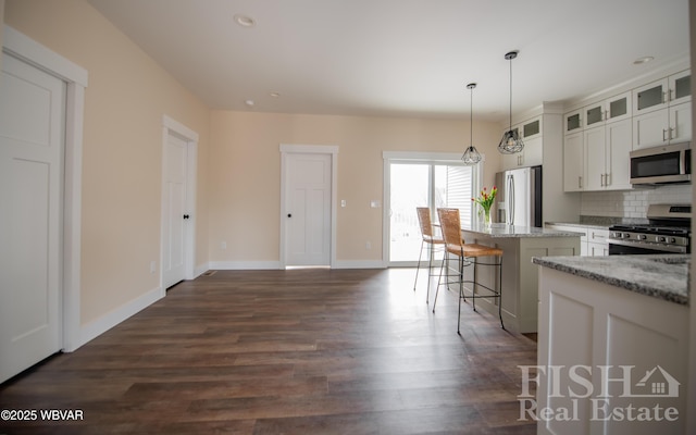 kitchen with glass insert cabinets, appliances with stainless steel finishes, light stone counters, decorative light fixtures, and white cabinetry