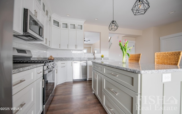 kitchen with light stone counters, decorative light fixtures, stainless steel appliances, white cabinetry, and a kitchen island