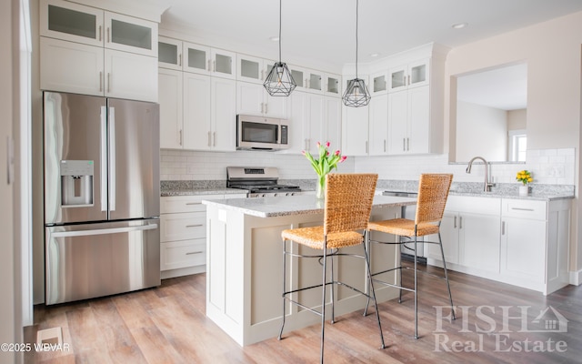 kitchen featuring glass insert cabinets, appliances with stainless steel finishes, light stone counters, a center island, and white cabinetry