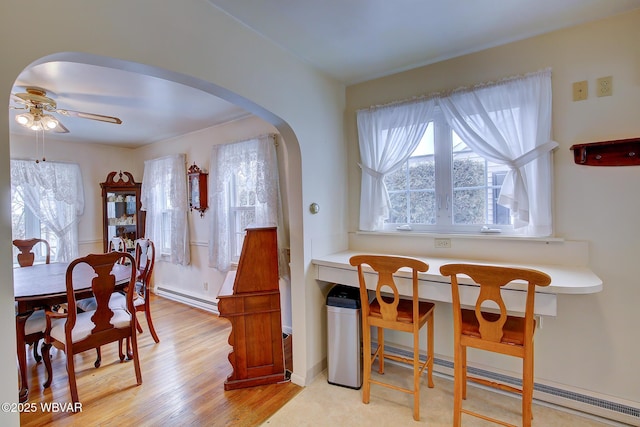 dining area with arched walkways, ceiling fan, baseboard heating, and light wood finished floors