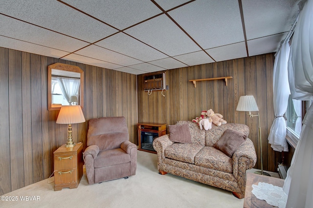 carpeted living room with wood walls, a wall mounted air conditioner, and a paneled ceiling