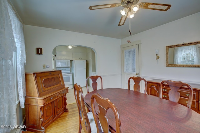 dining room with arched walkways, ceiling fan, and light wood-style flooring