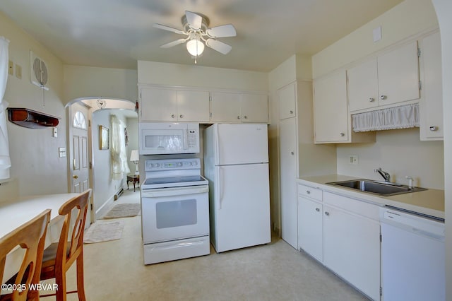 kitchen featuring white appliances, arched walkways, white cabinets, light countertops, and a sink