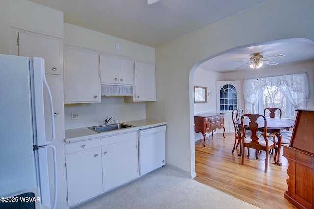 kitchen with arched walkways, white appliances, a sink, white cabinetry, and light countertops