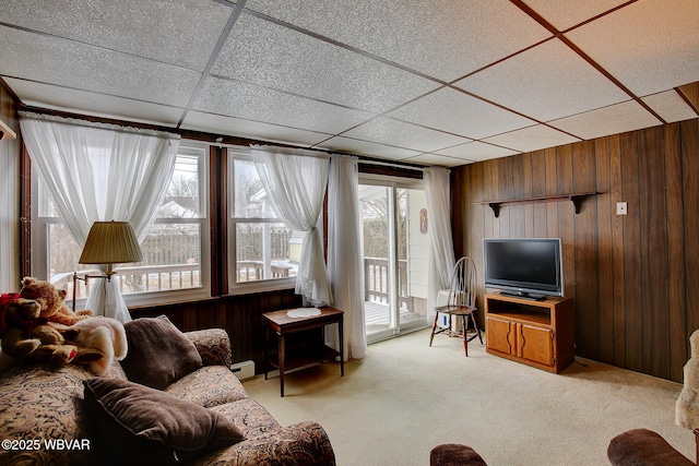 living area featuring light carpet, a baseboard radiator, wooden walls, and a drop ceiling