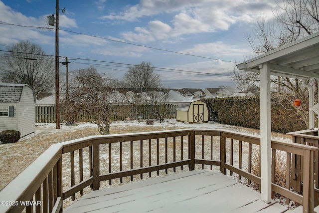 snow covered deck with an outdoor structure, fence, and a storage unit