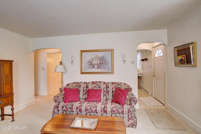 living room featuring arched walkways, a baseboard radiator, baseboards, and light colored carpet